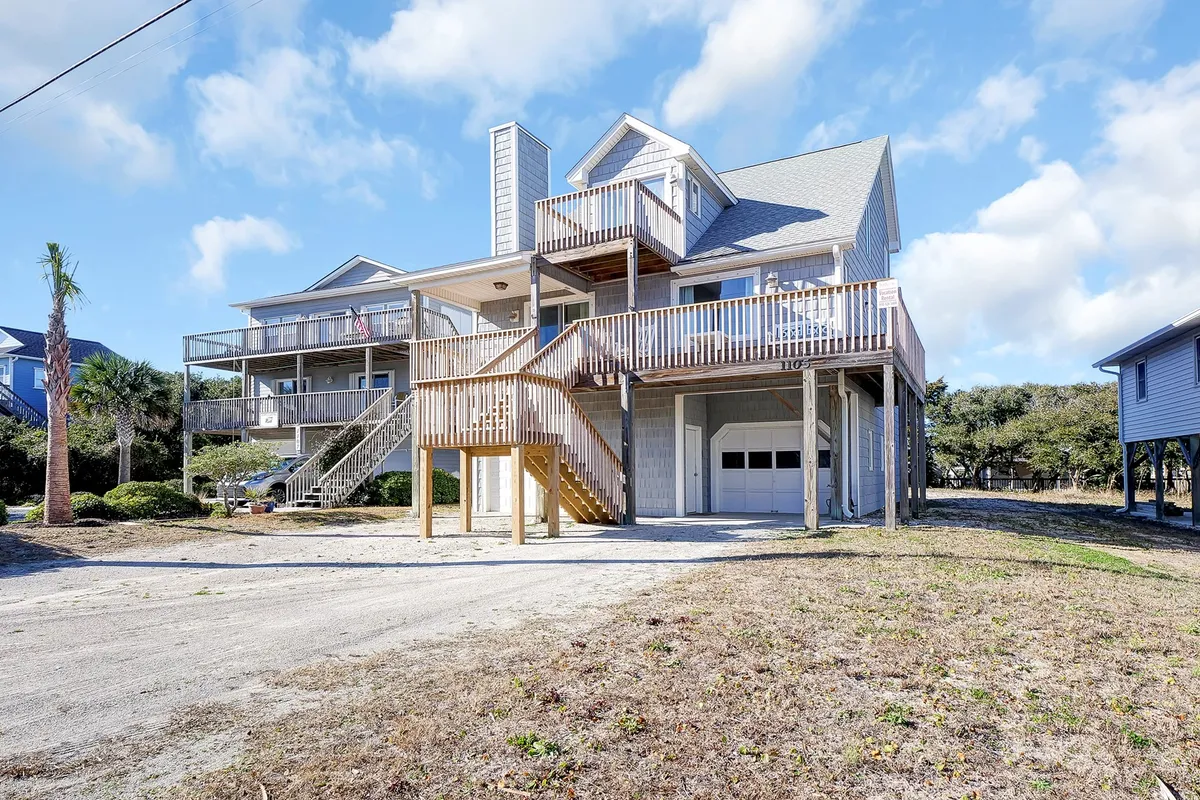 An exterior view highlighting the house's deck areas bordered by palm trees, emphasizing vibrant outdoor living. The deck provides ample space for gatherings, dining, and relaxing, with natural surroundings that reinforce the coastal atmosphere.
