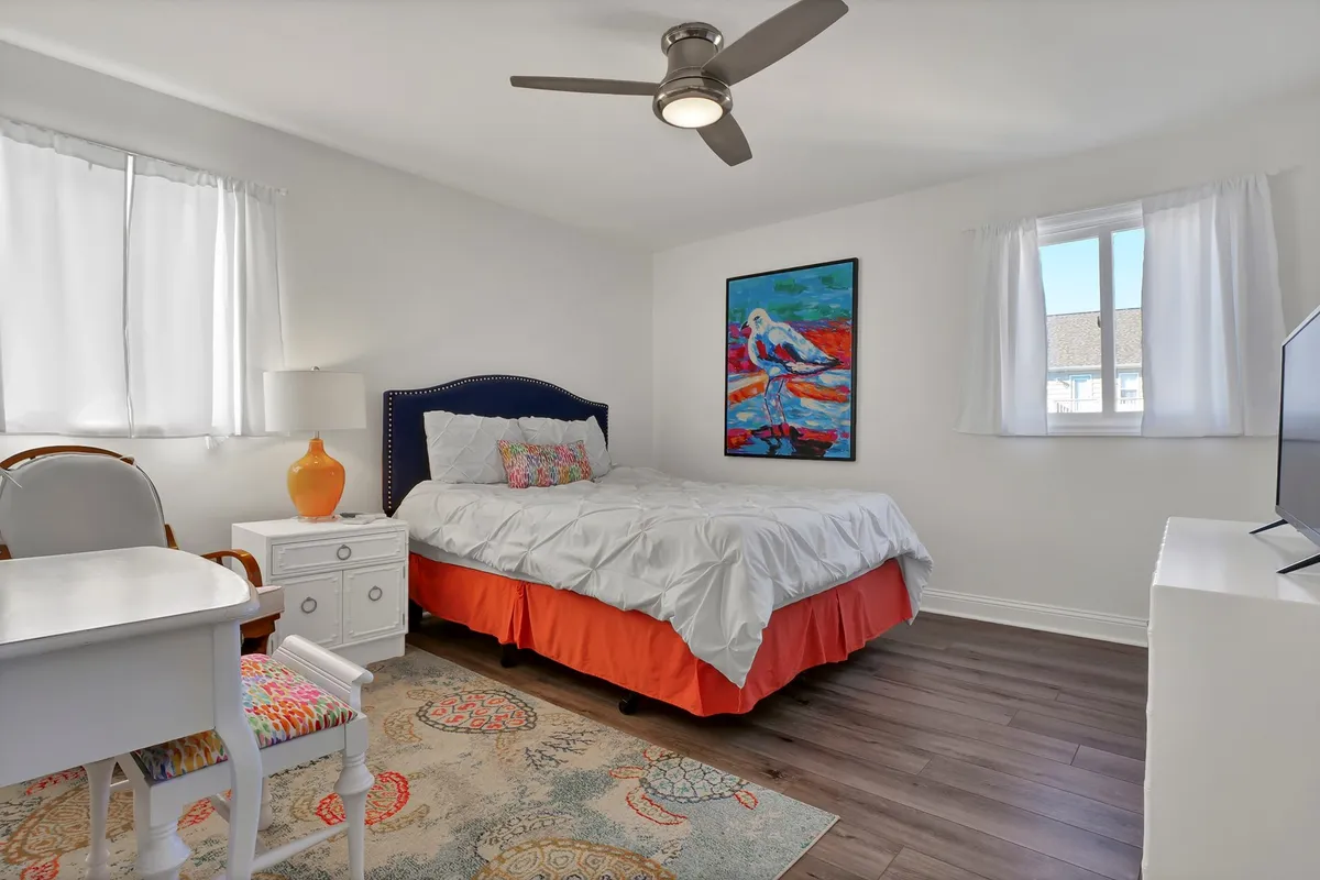 A cozy bedroom with a bed dressed in colorful bedding, complemented by a desk and a decorative chair. The setup suggests comfort and versatility, ideal for guests with children who may require extra sleeping arrangements or a quiet space.