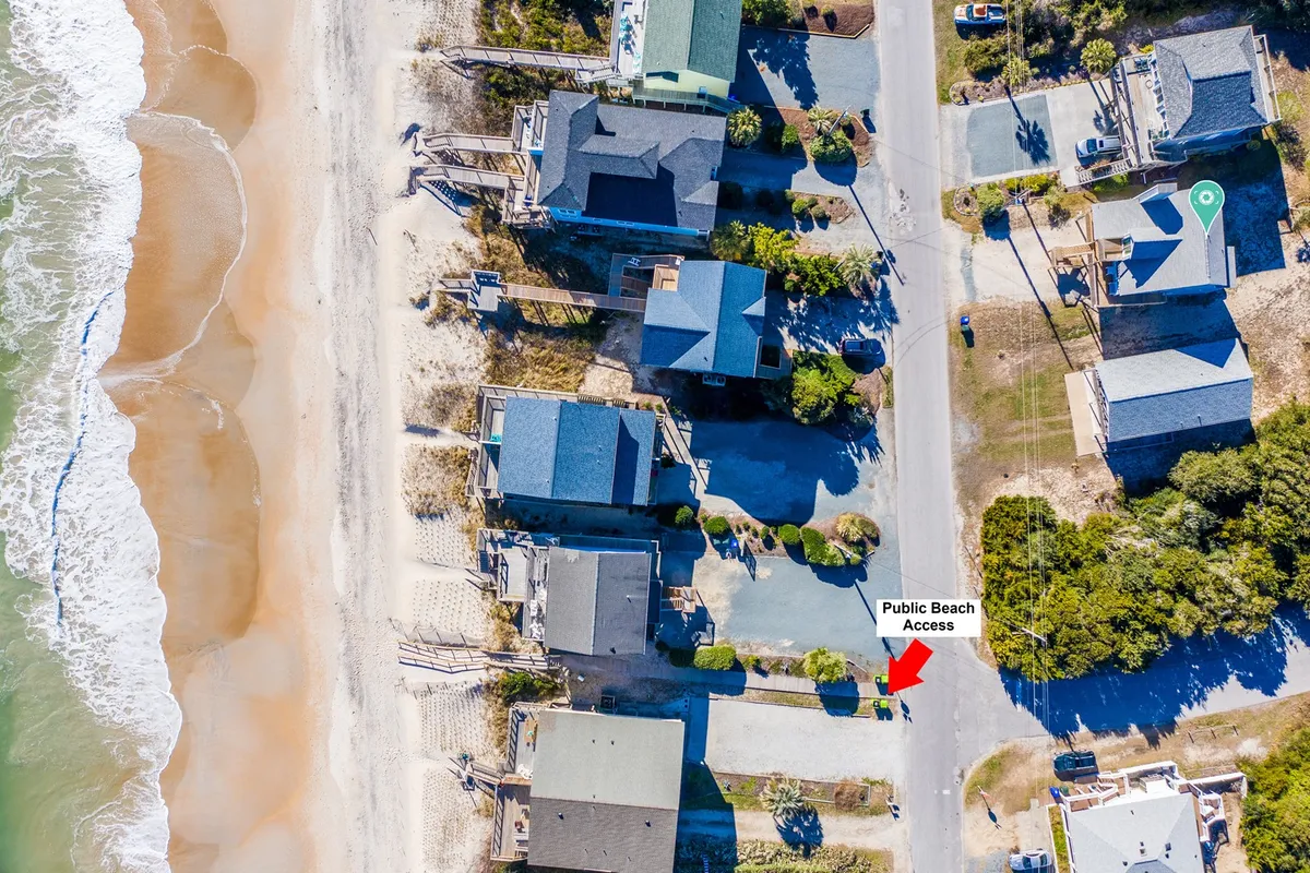This image showcases the direct beach access, with a clear view of the pathway leading from a row of houses across the street toward the ocean waves. The sandy shoreline and the proximity to the water exemplify the property's easy access to one of Topsail Island’s best features.