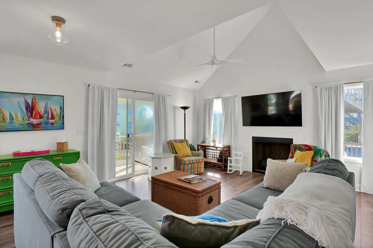 A spacious living room is centered around a large sectional sofa and adorned with colorful artwork and a wooden coffee table. A flat-screen TV is positioned for movie nights, while abundant sunlight streams through the windows, creating a cheerful and comfortable setting for relaxation and socializing.
