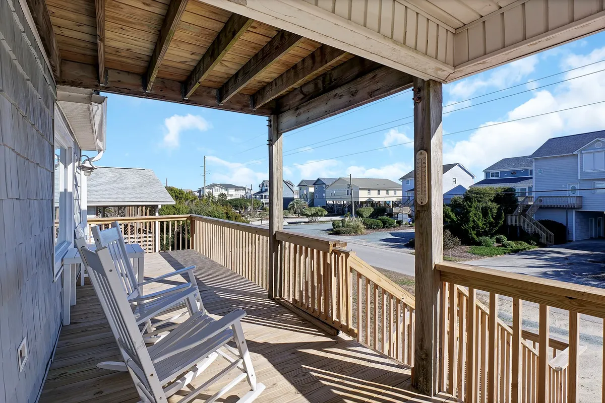 A tranquil exterior scene featuring wooden rocking chairs on a veranda, overlooking the street through a classic railing. This inviting perspective highlights a communal porch perfect for sipping coffee, hosting barbecues, or watching children play, evoking relaxed, shared moments.