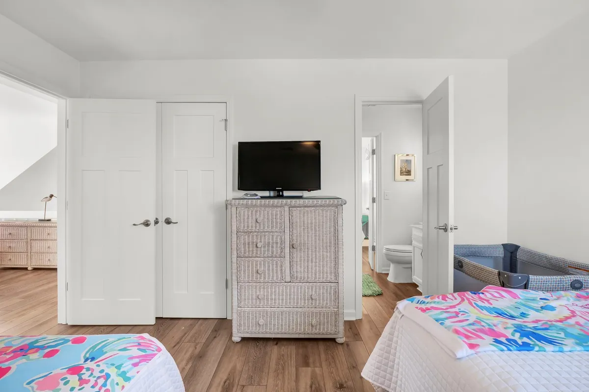 A cheerful bedroom with colorful bedding, a wicker dresser, a wall-mounted TV, and doors opening onto other spaces. The room feels both playful and connected, with decor that appeals to younger guests or families.