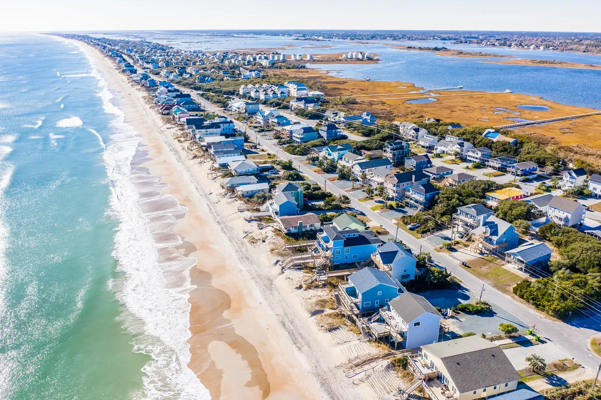 A wide, scenic view of the beachfront, houses, ocean, marshland, and the road connecting everything. It highlights the vibrant intersection of the community, beach, and natural landscape, reinforcing the family-friendly, accessible seaside lifestyle.