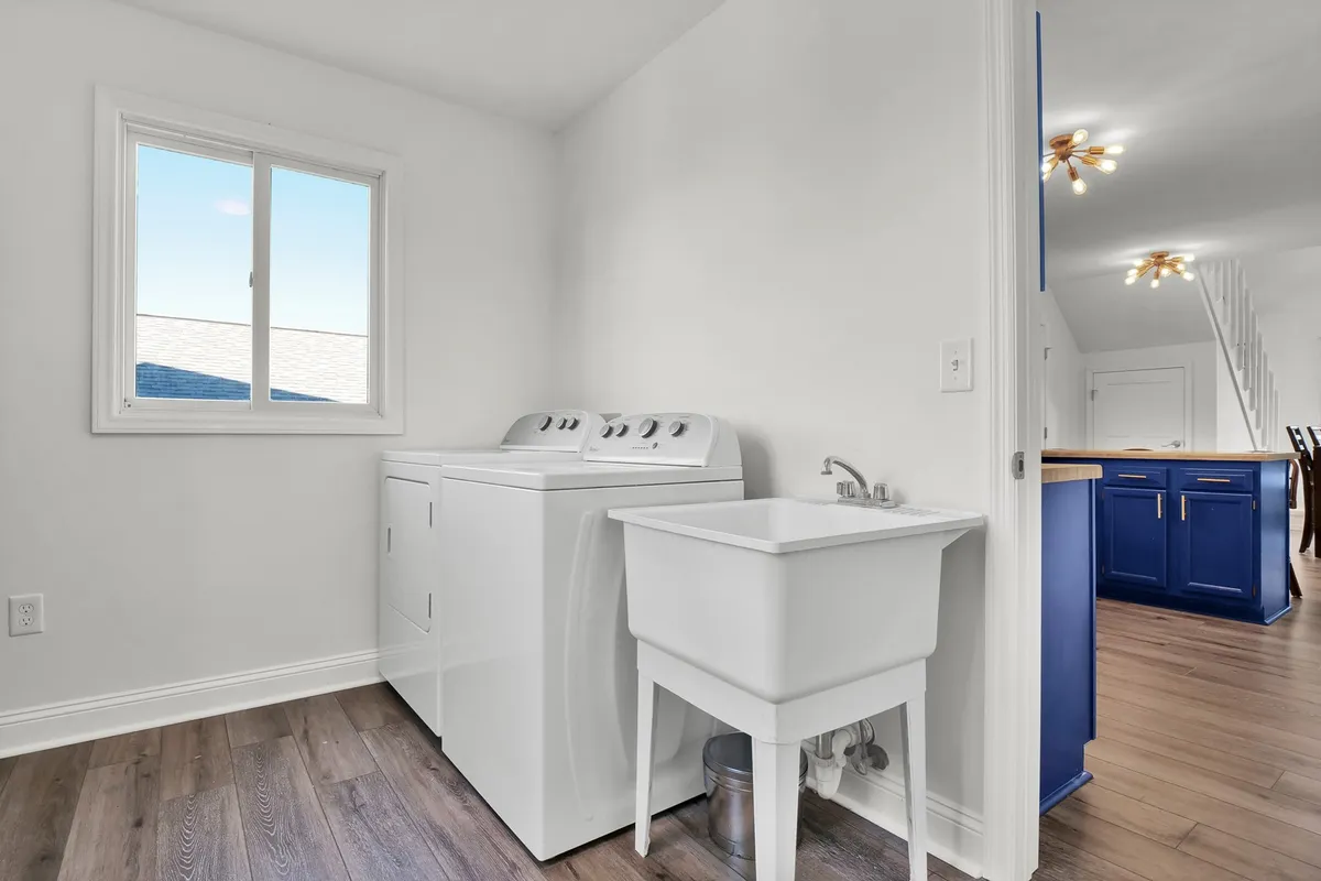 A well-lit laundry room featuring a modern washing machine, a utility sink, and a window that fills the space with natural light. The layout is clean and practical, emphasizing ease of use for daily chores.
